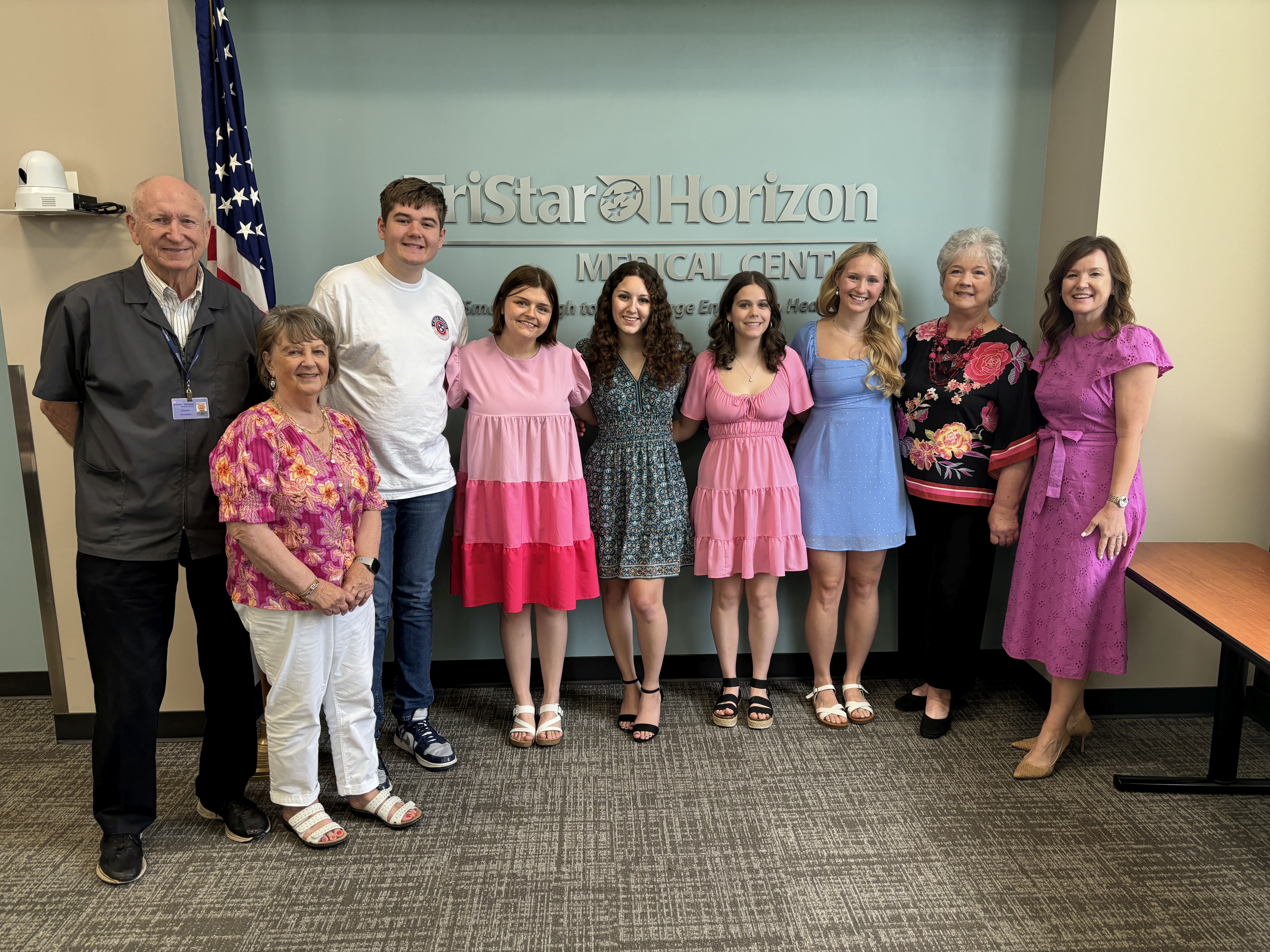Five of ten high school students stand with three volunteer committee members and hospital CEO