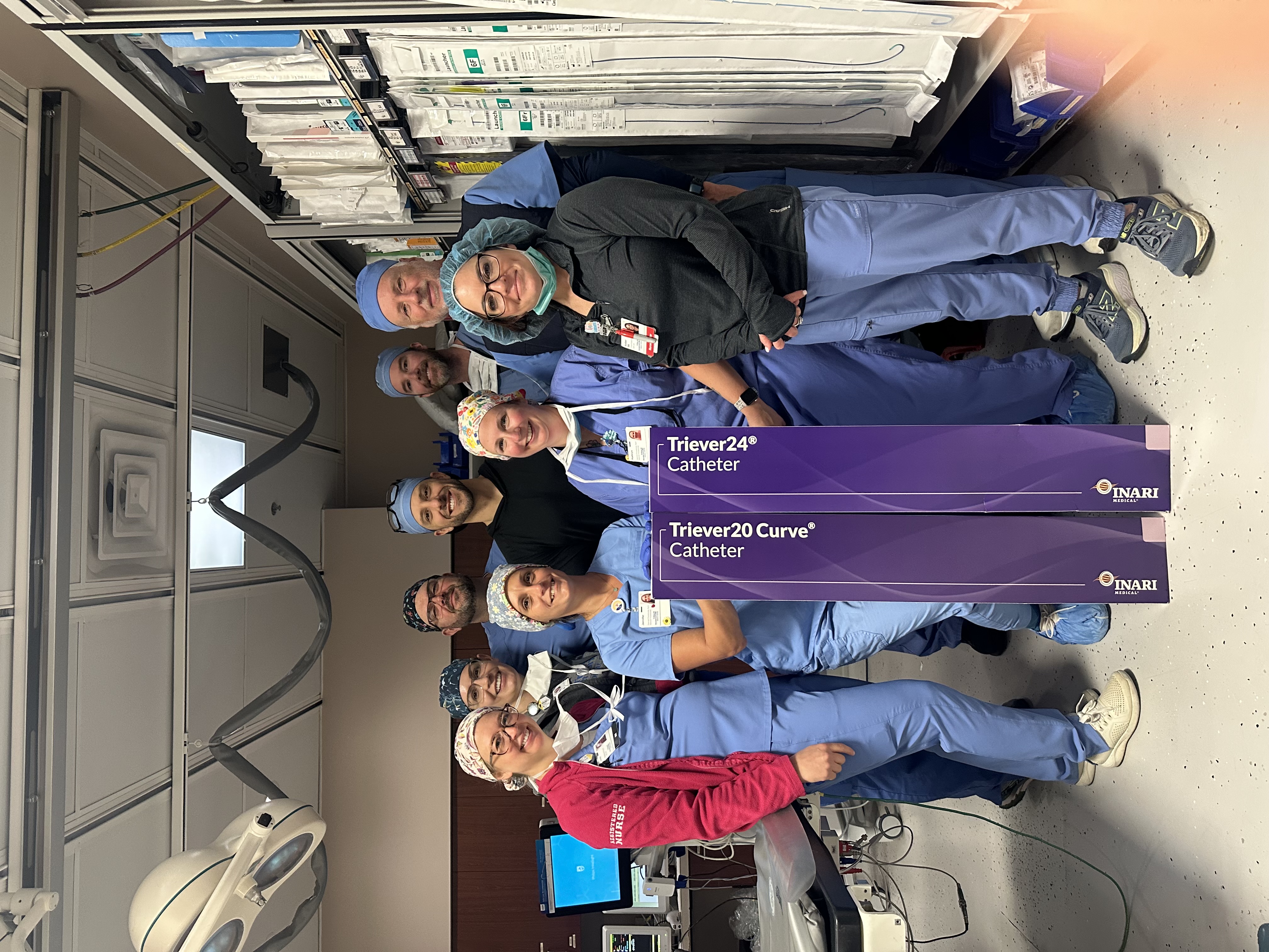 First Pulmonary Thrombectomy Team poses with banners in operating room.