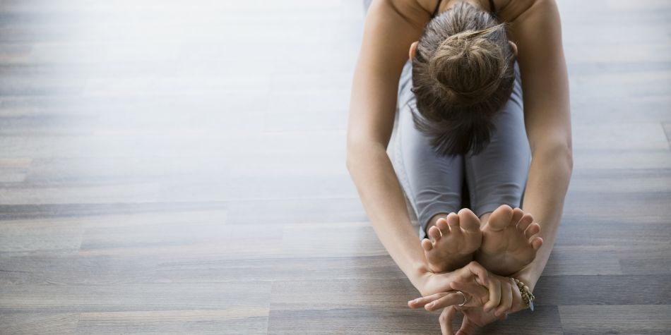 A woman in seated forward bend practicing mudra yoga, reaching her hands over her toes.