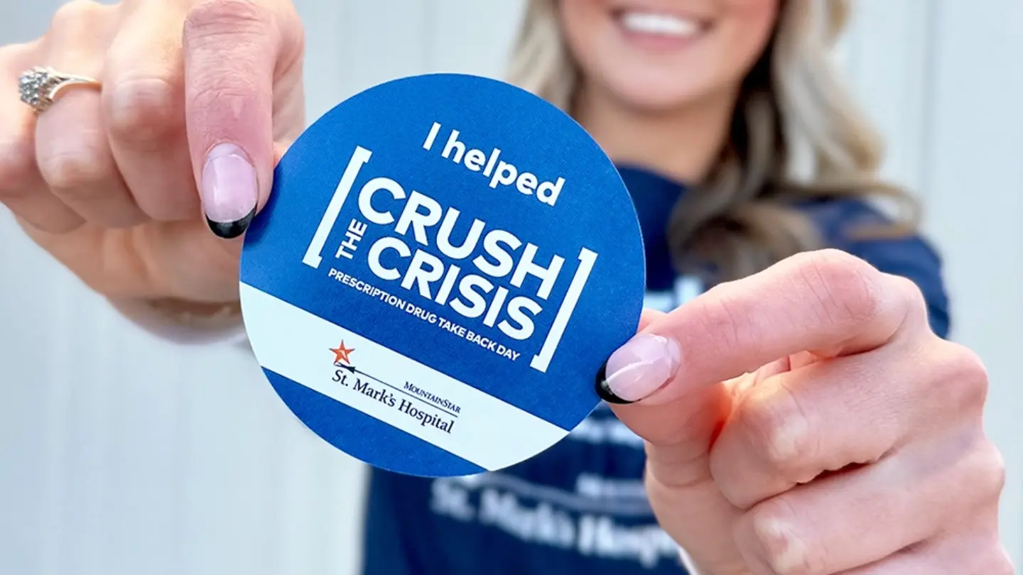 A Crush the Crisis sticker is held up to the camera by a woman who is slightly out of focus.