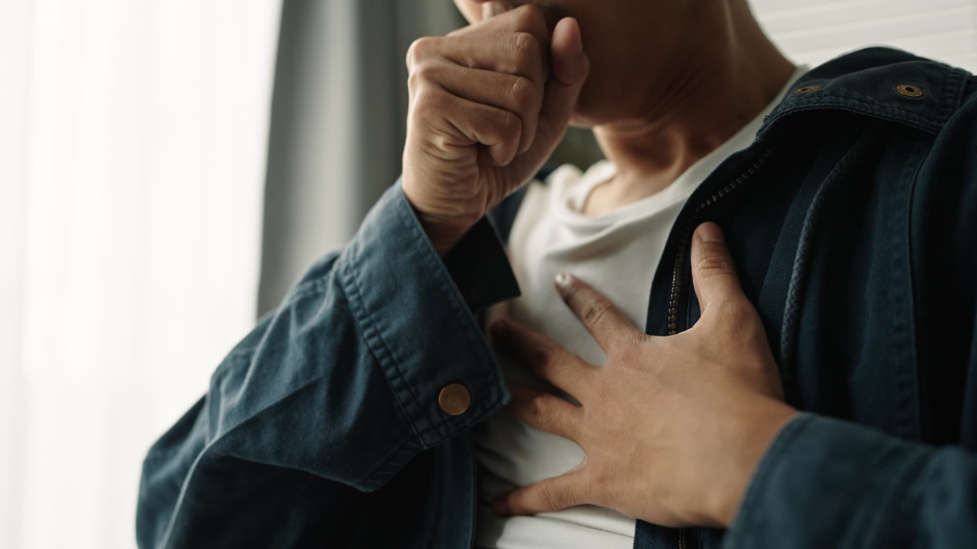A man holds his hand to his chest while covering his mouth and coughing.