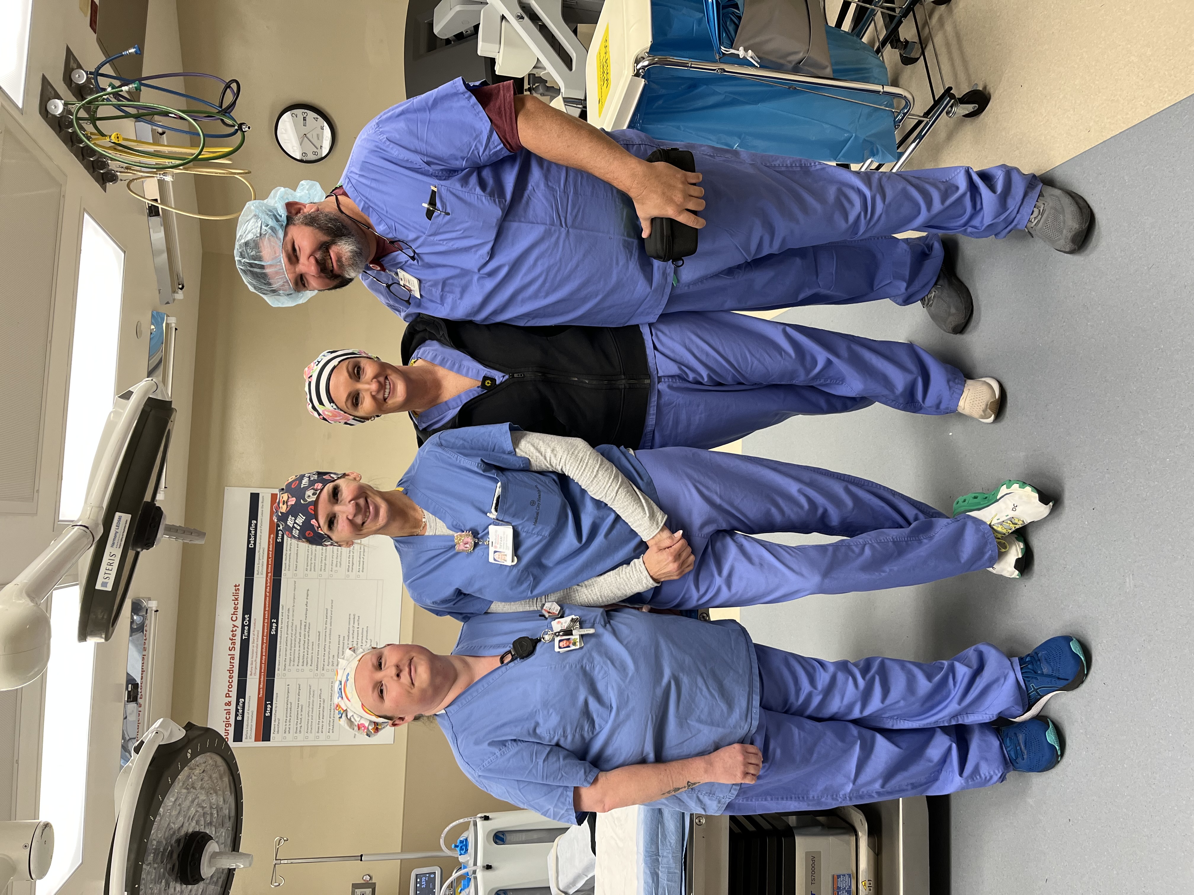 Four surgeons standing in the operating room, smiling for a group photo.