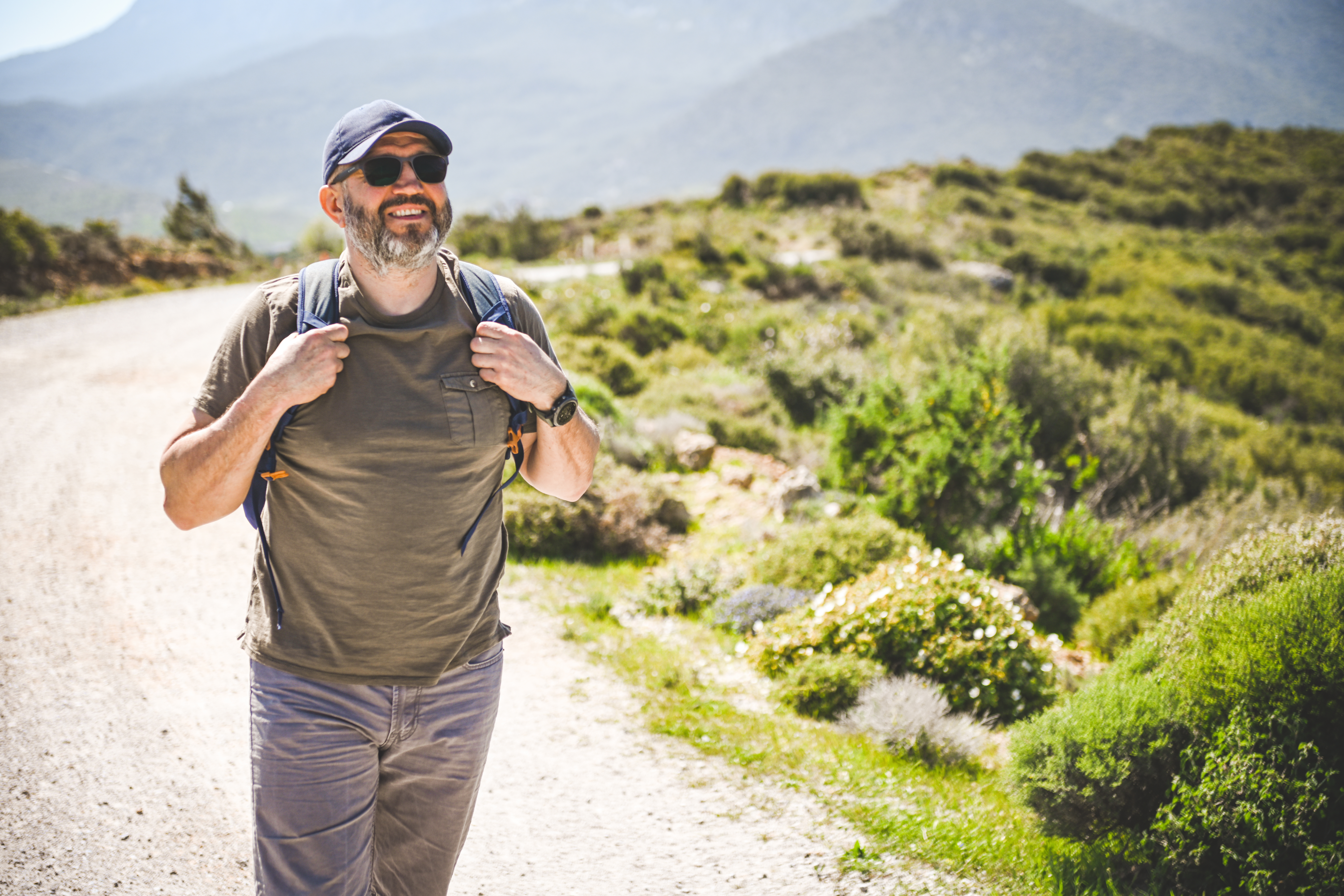 Mature adult smiling man hiking down a gravel road outdoors