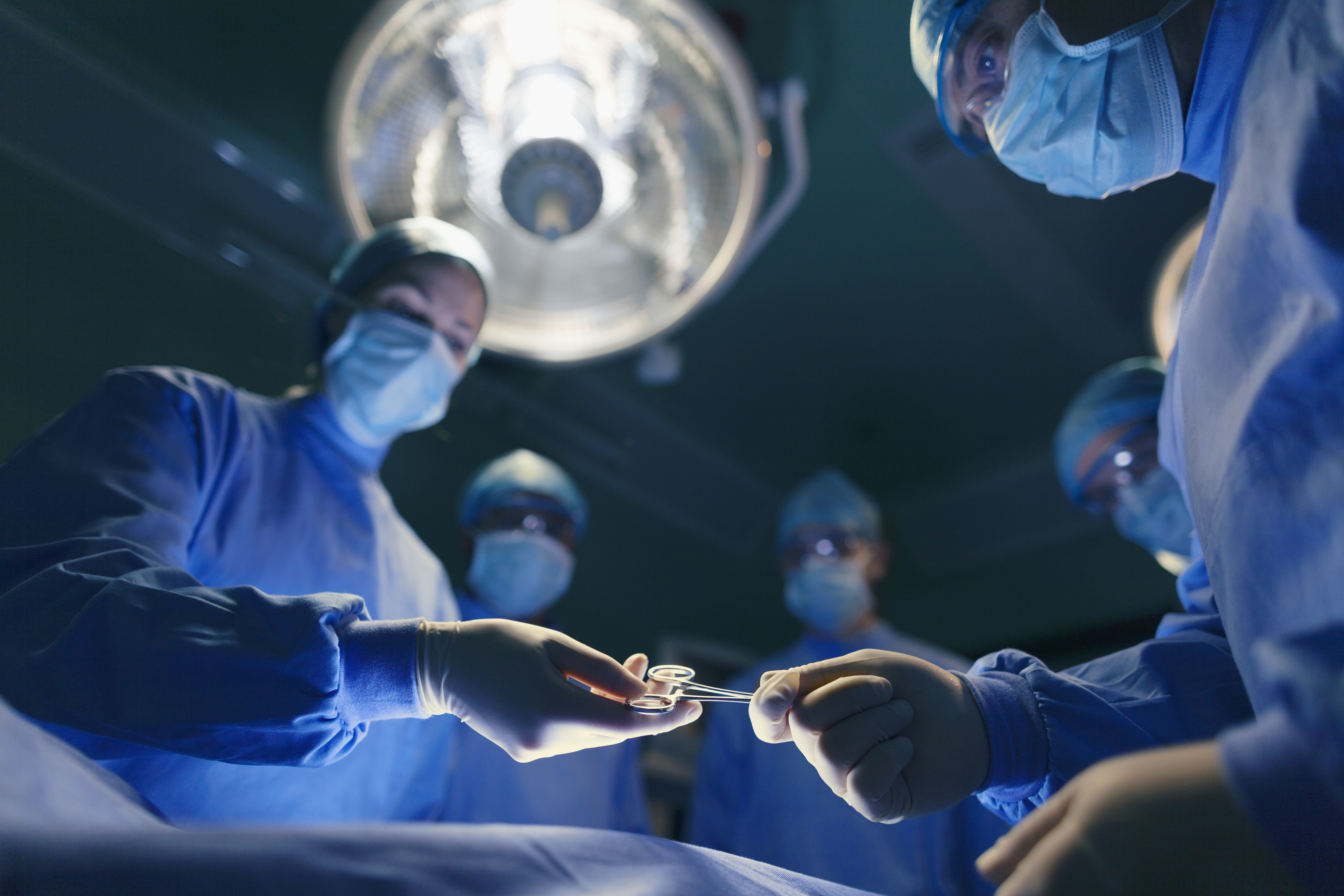 Surgical staff in scrubs performing a procedure on a patient in an operating room.