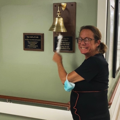 A woman smiles while ringing a bell in a hospital hallway on her last day of treatment.