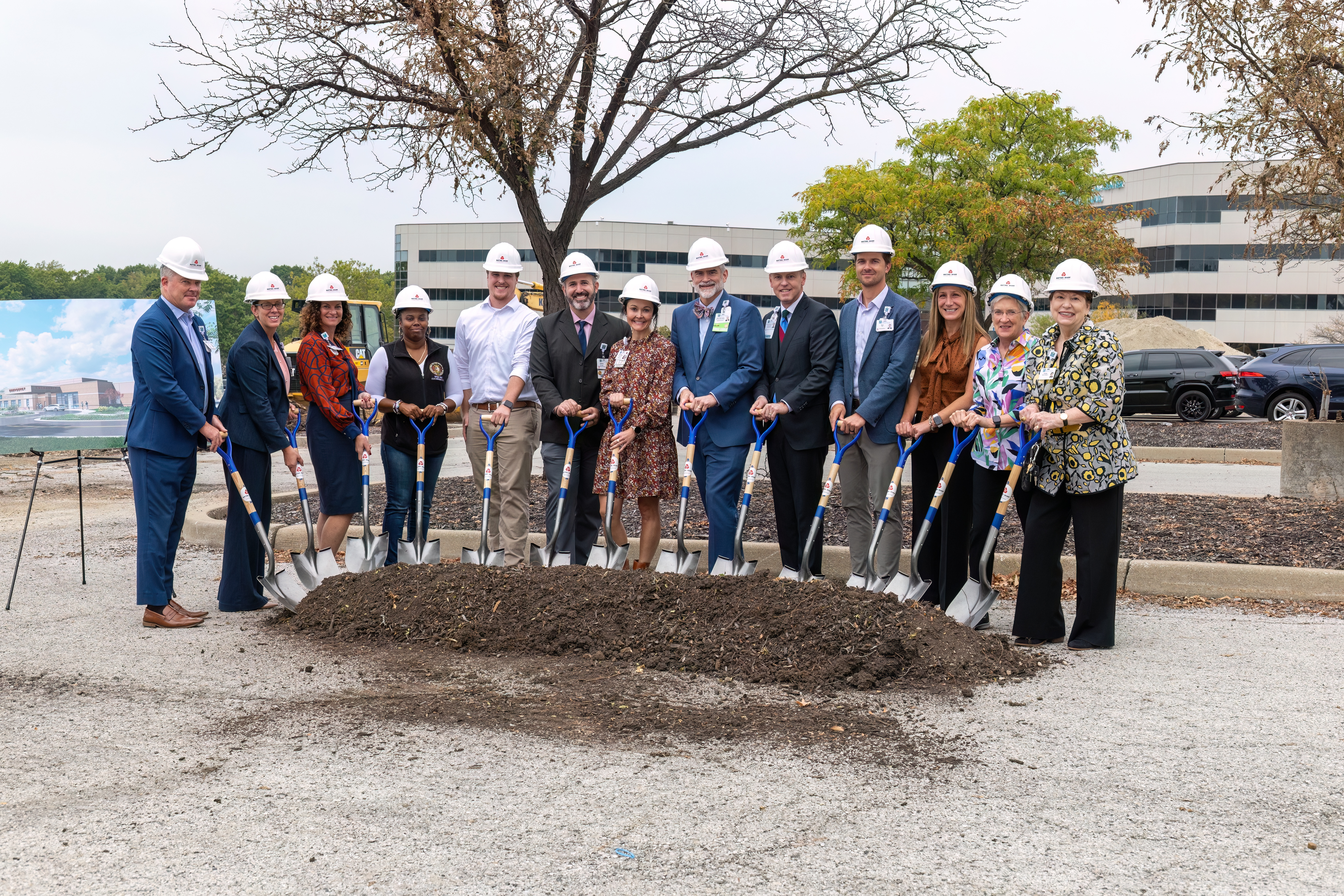 HCA team members wearing hardhats and holding ceremonial shovels pose with dirt pile at groundbreaking ceremony.