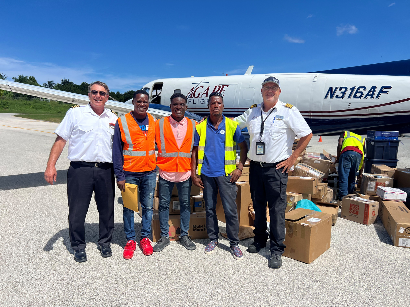Five men stand with boxes and a plane behind them.