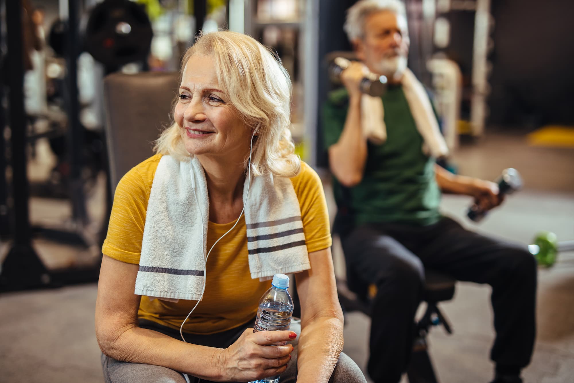 Senior woman holding a water bottle and taking a break from her workout at the gym.