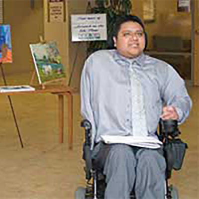 Emmanuel Martinez smiles while sitting in front of a several paintings.