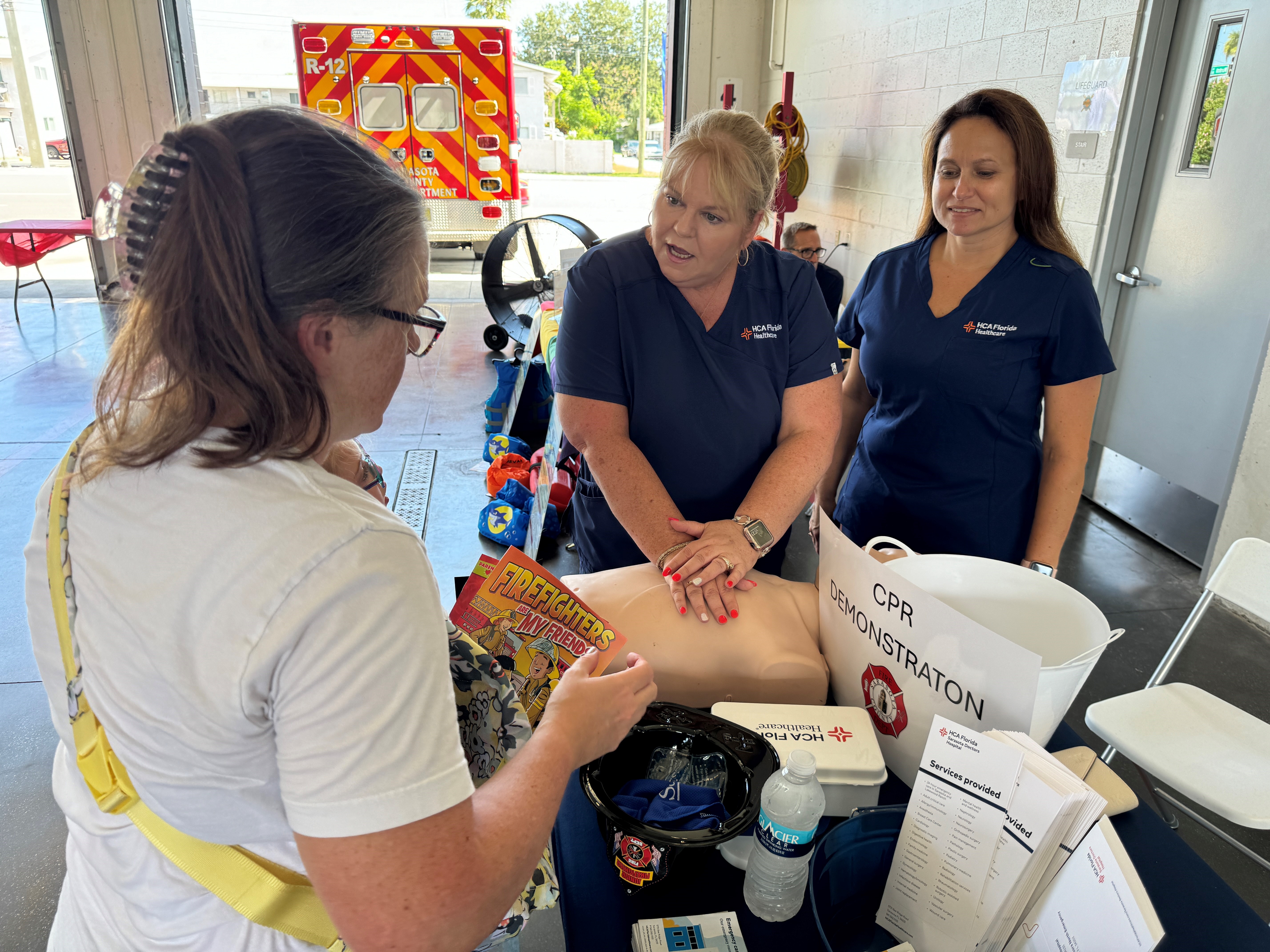 Nurses put their hands on a mannequin. Woman watches.