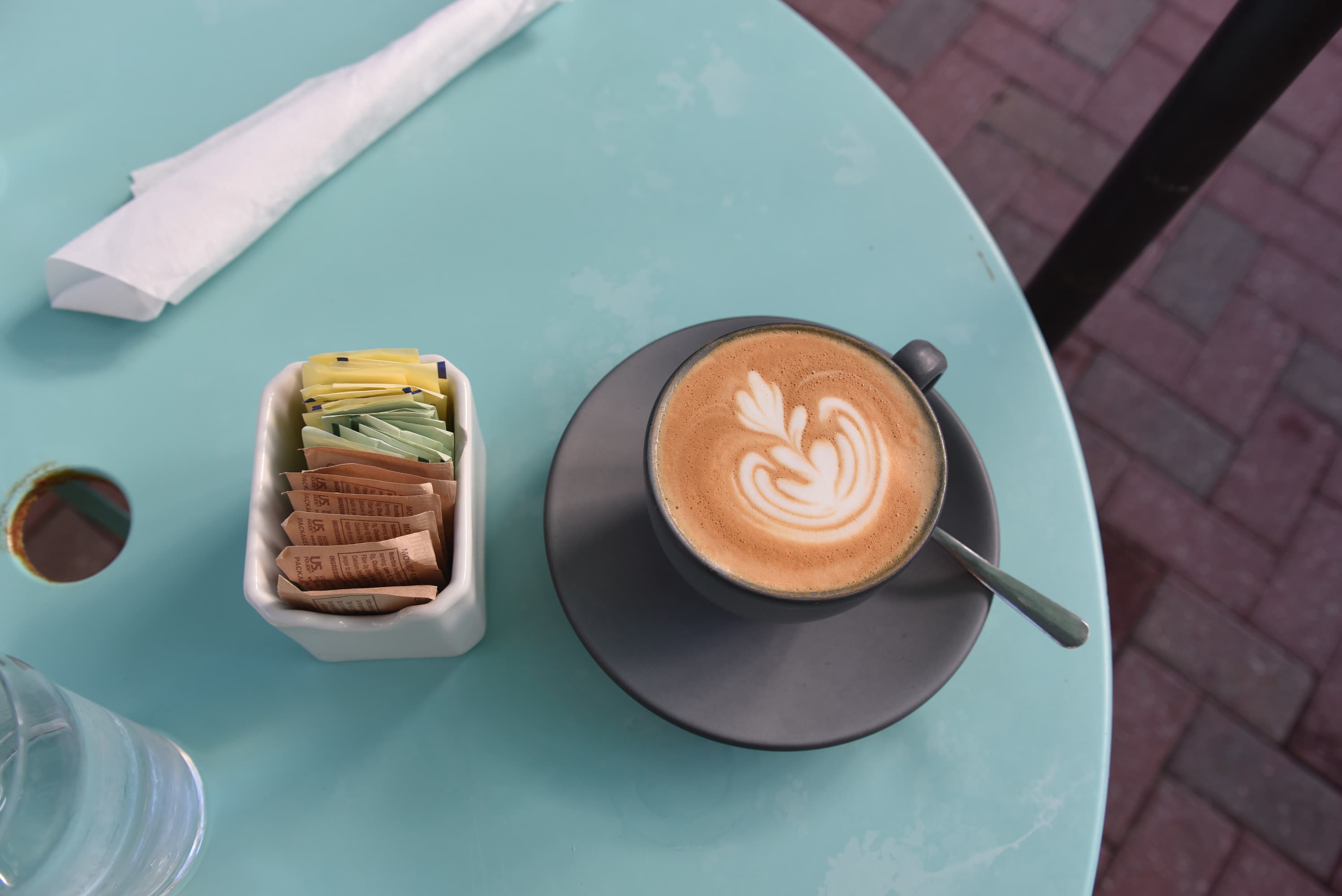 A fancy cappuccino and sweetener packets on a café table.