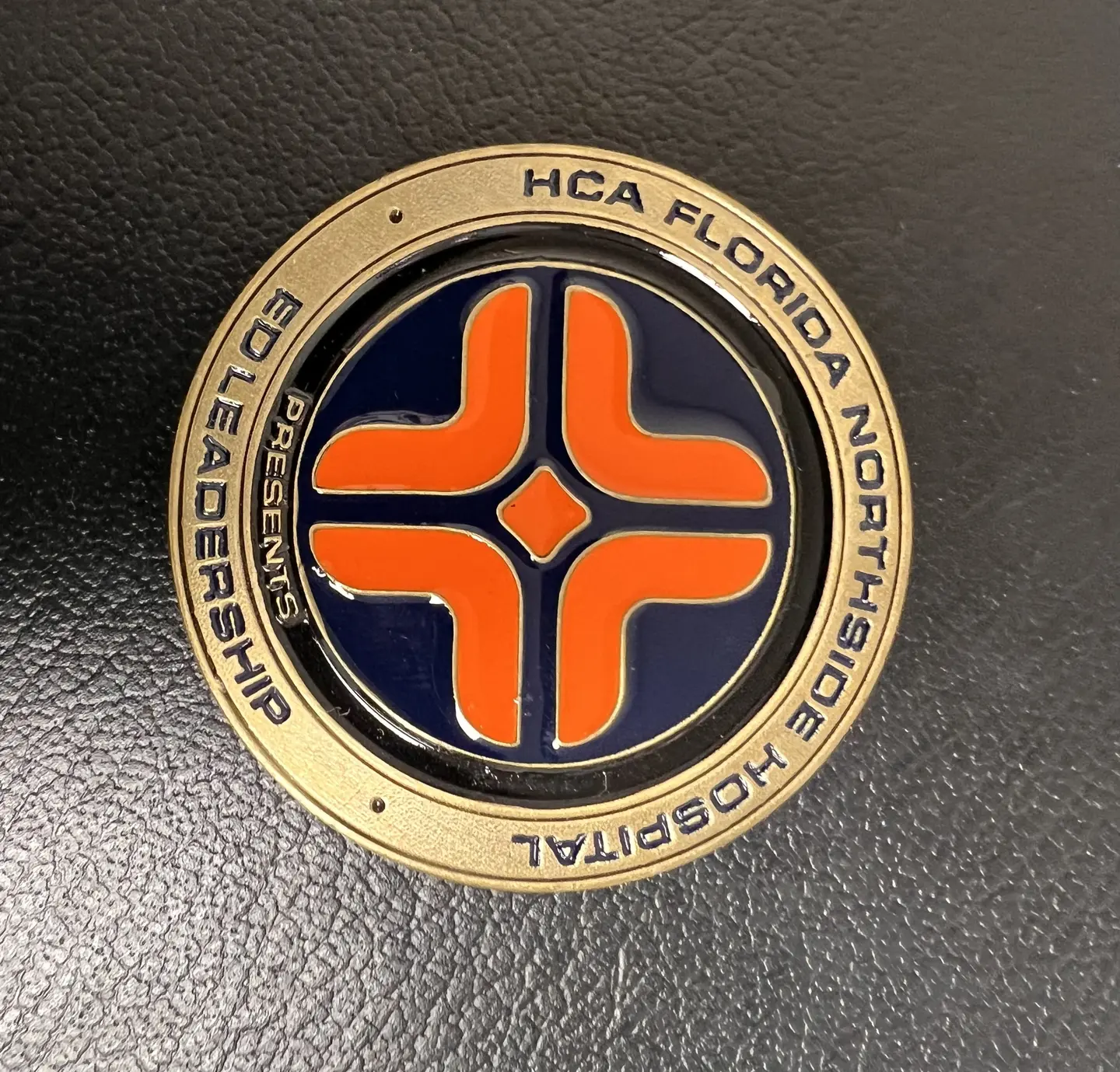 Gold coin engraved along its edge with "HCA Florida Northside Hospital Challenge Coin ED Leadership" and orange HCA emblem in its center.