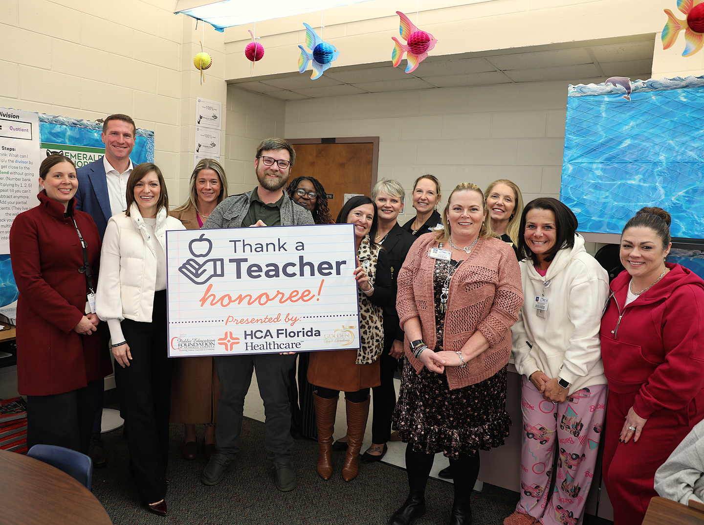 Matthew Andres&nbsp;holding a banner for thank a teacher award with his coworkers inside a classroom.
