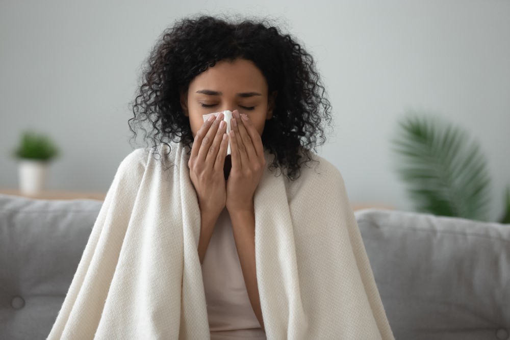 A woman wrapped in a blanket blows her nose into tissue
