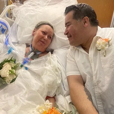 Lori in her hospital bed wearing a veil and wedding gown; Eddie, her husband, snuggles up beside her.