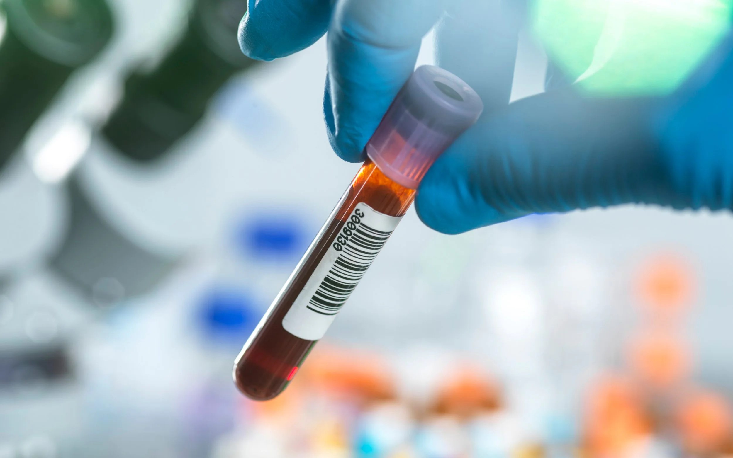 A close-up of fingers holding a collection tube full of blood.