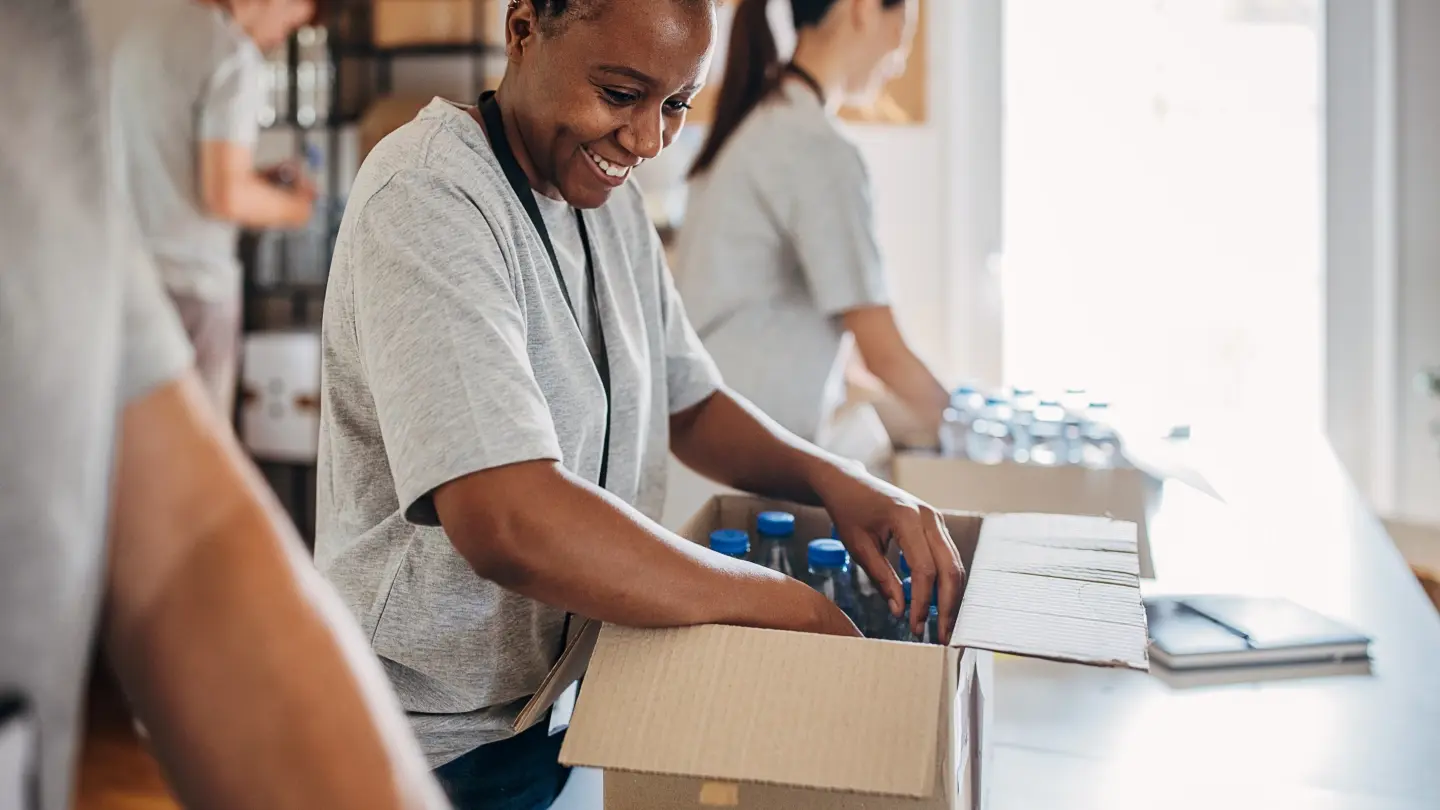 A smiling young woman volunteers her time packing necessities and emergency supplies into boxes.