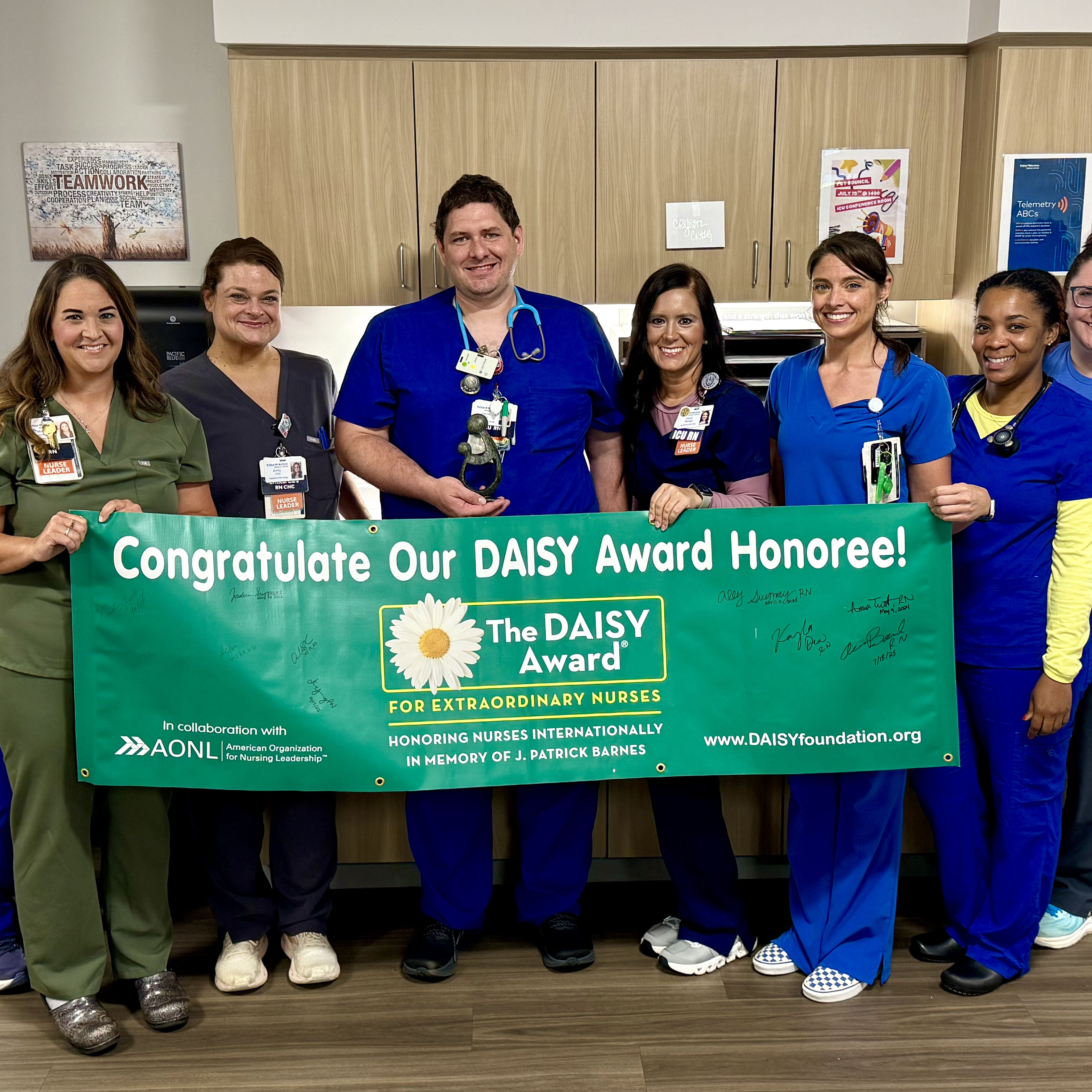 ICU Nurse Aaron Bond holding a daisy award banner with the other members of the ICU
