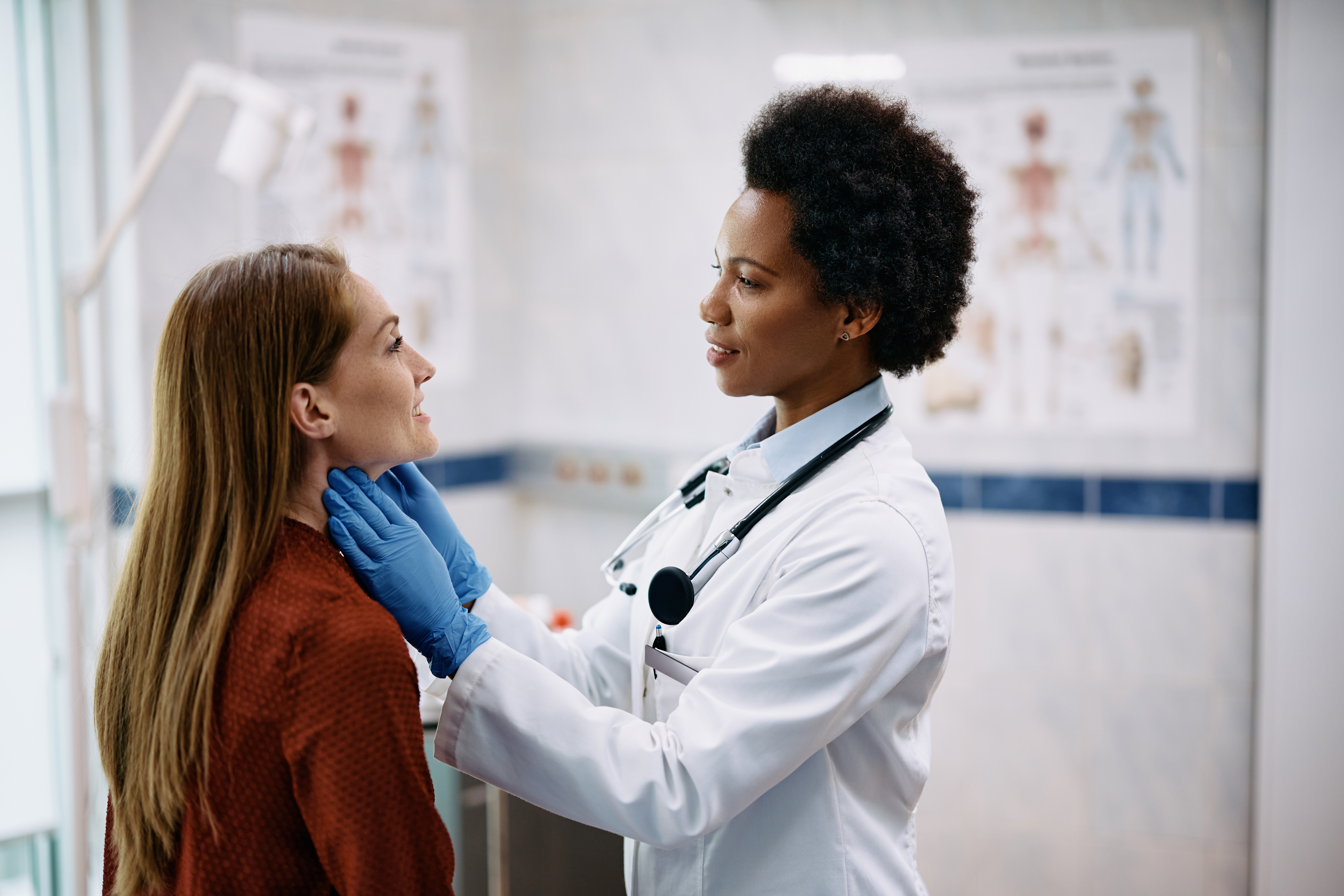 A smiling woman having her thyroid examined by an endocrinologist in a clinical setting.