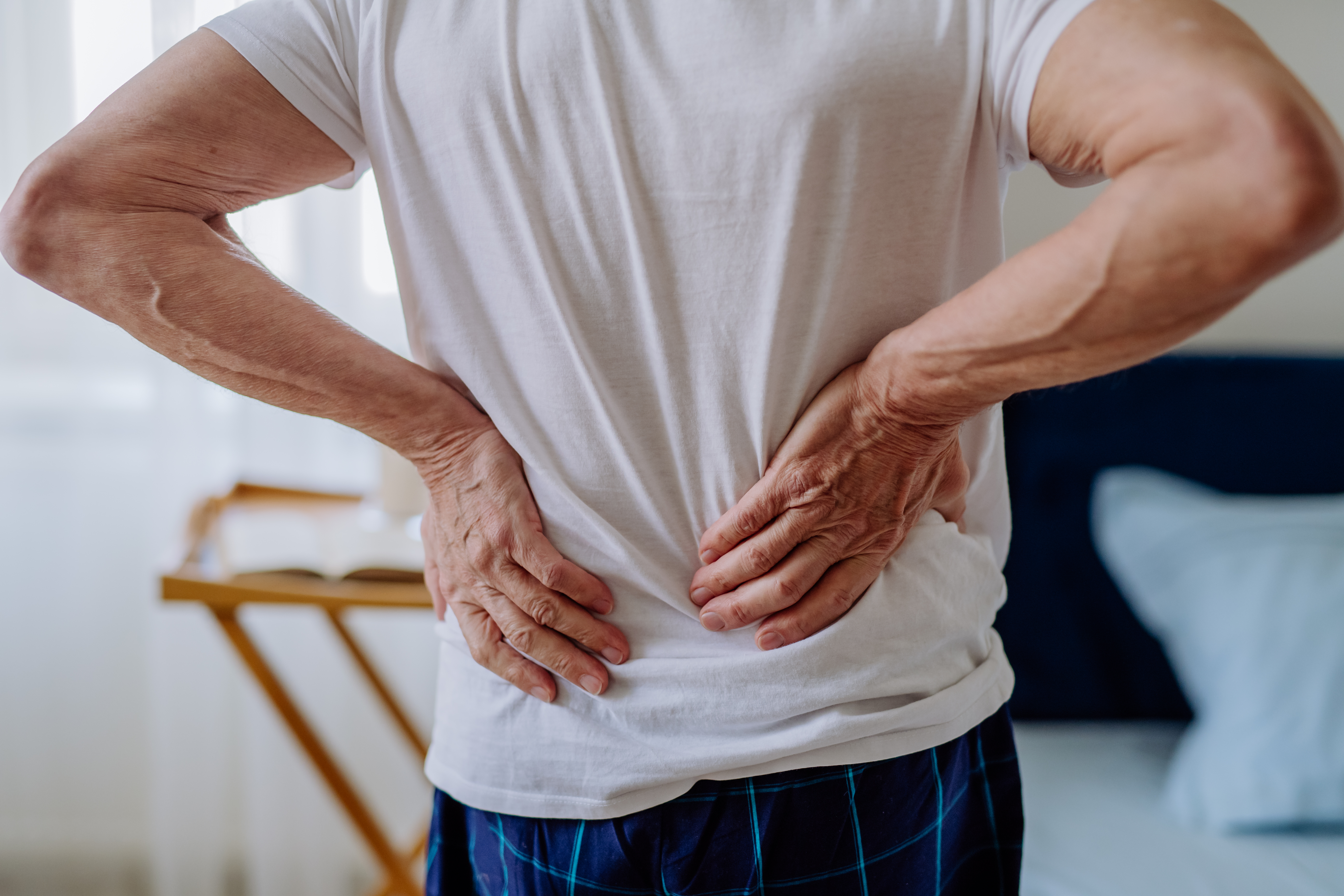 Man having back pain, standing in his bedroom