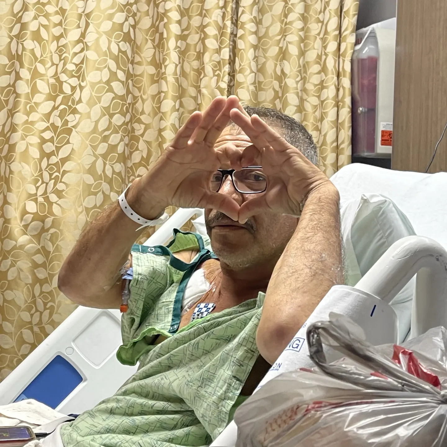 Itzel Guzman's father in hospital bed making a heart shape with his hands