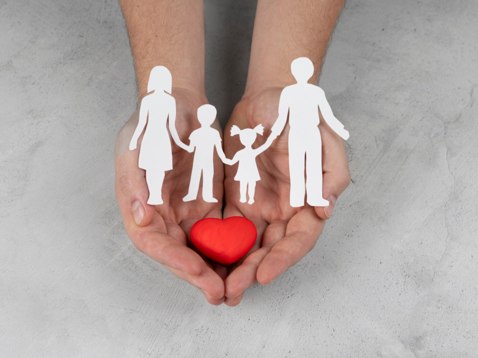 Holding a paper cut out of a family and a heart in their hands.