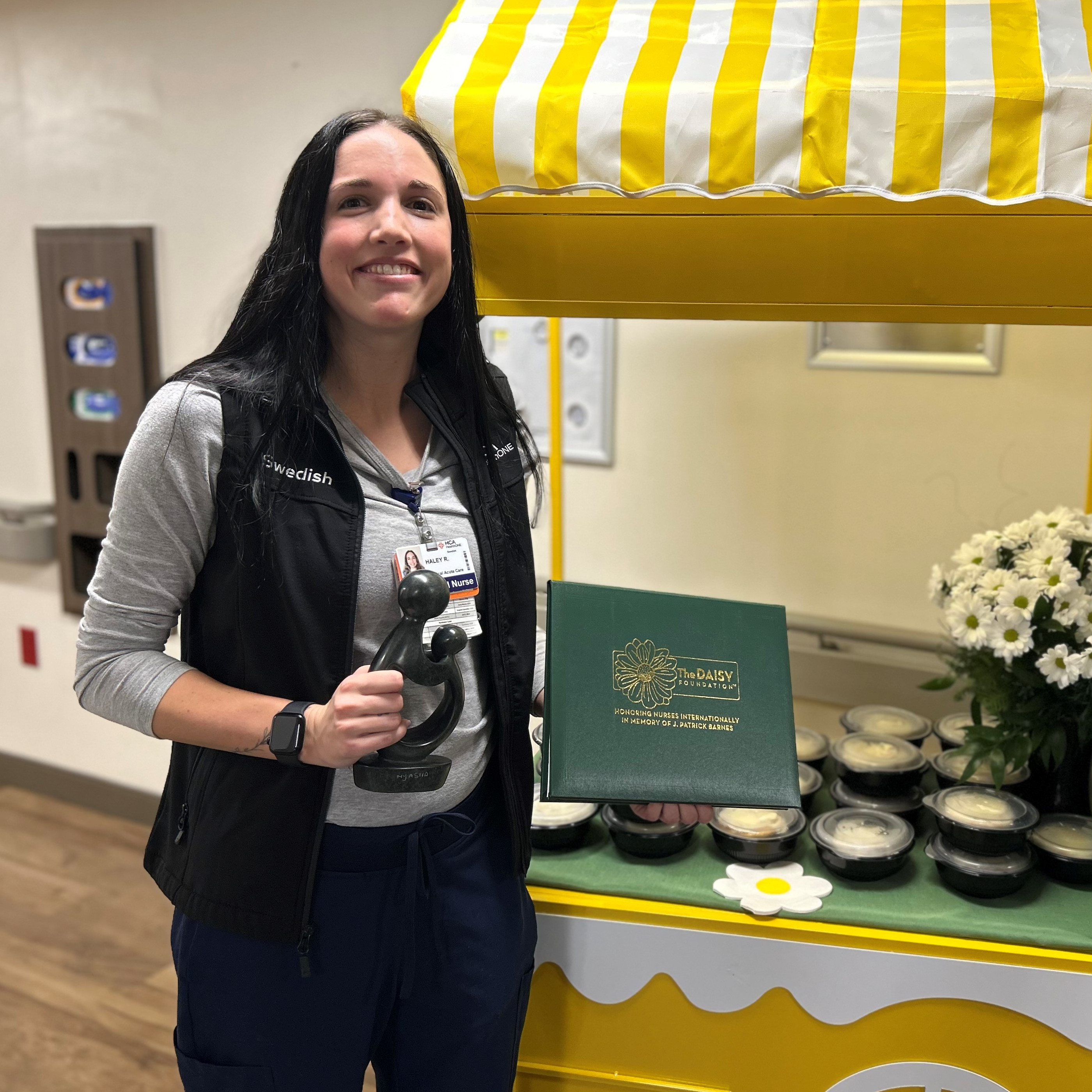 Haley Roberts holding her Daisy reward and the certificate, while smiling for the photo.