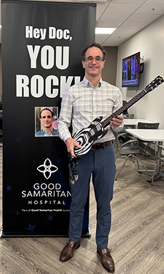 Award winner Dr. Gary Gechlik holding a guitar, in front of a "Hey Doc, You Rock" banner.