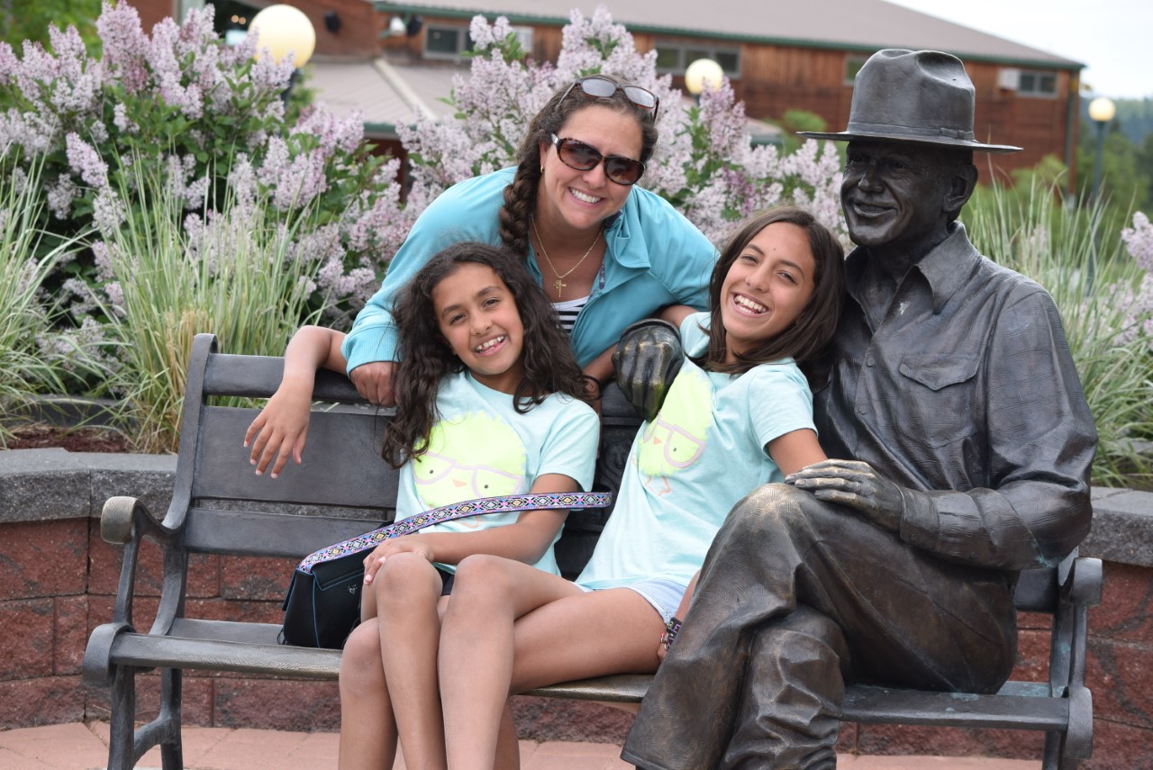 Breast cancer survivor Whitney and her two daughters smile, while sitting on a bench.