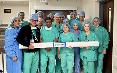 The cardiac care team at Los Robles Hospital posing for a picture with a long, white board, with the Pi-Cardia ShortCut device name on it.