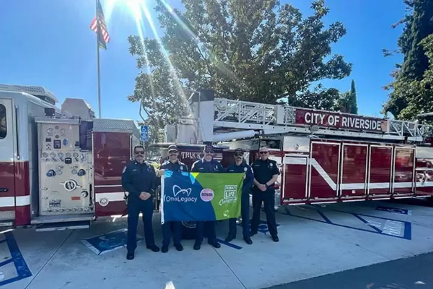Members of the Riverside Fire Department smile while standing in front of a fire engine, holding a Donate Life flag.