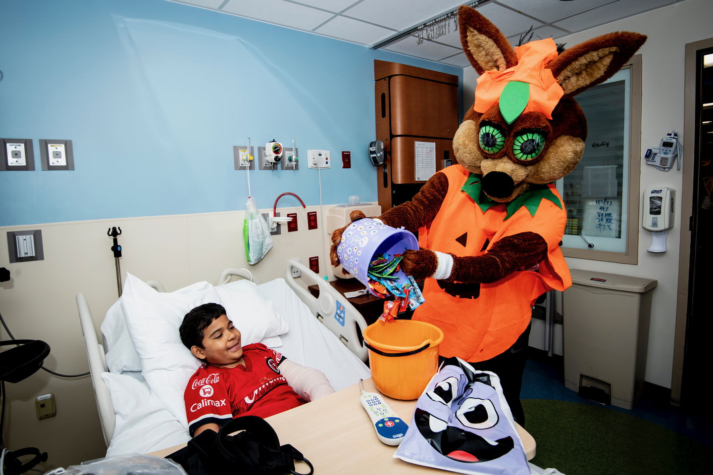 San Antonio Spurs Coyote giving out candy to a patient laying in a hospital bed.