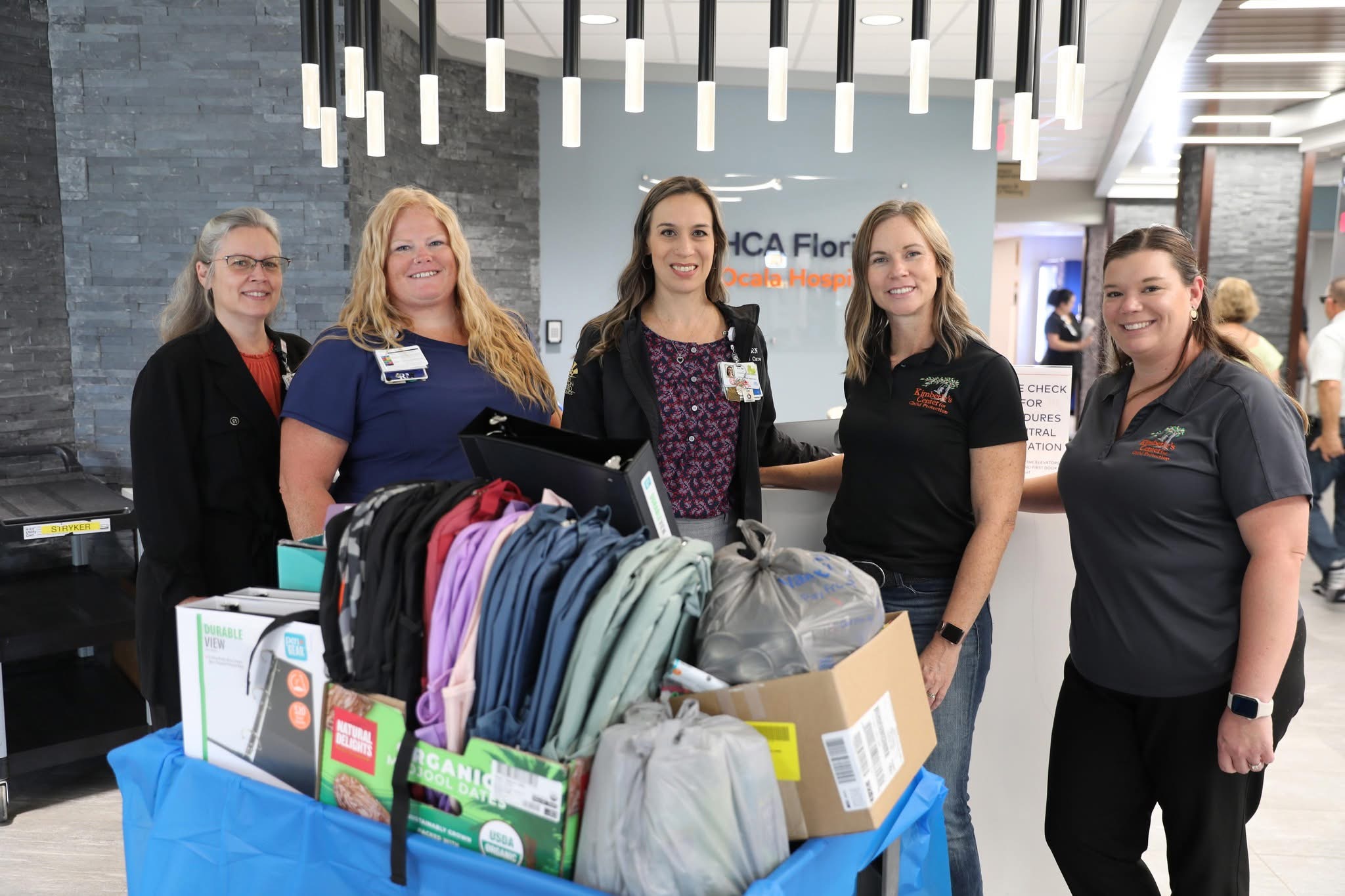 Hospital nurses and leadership smile with nonprofit leaders next to a wagon of children's supplies.