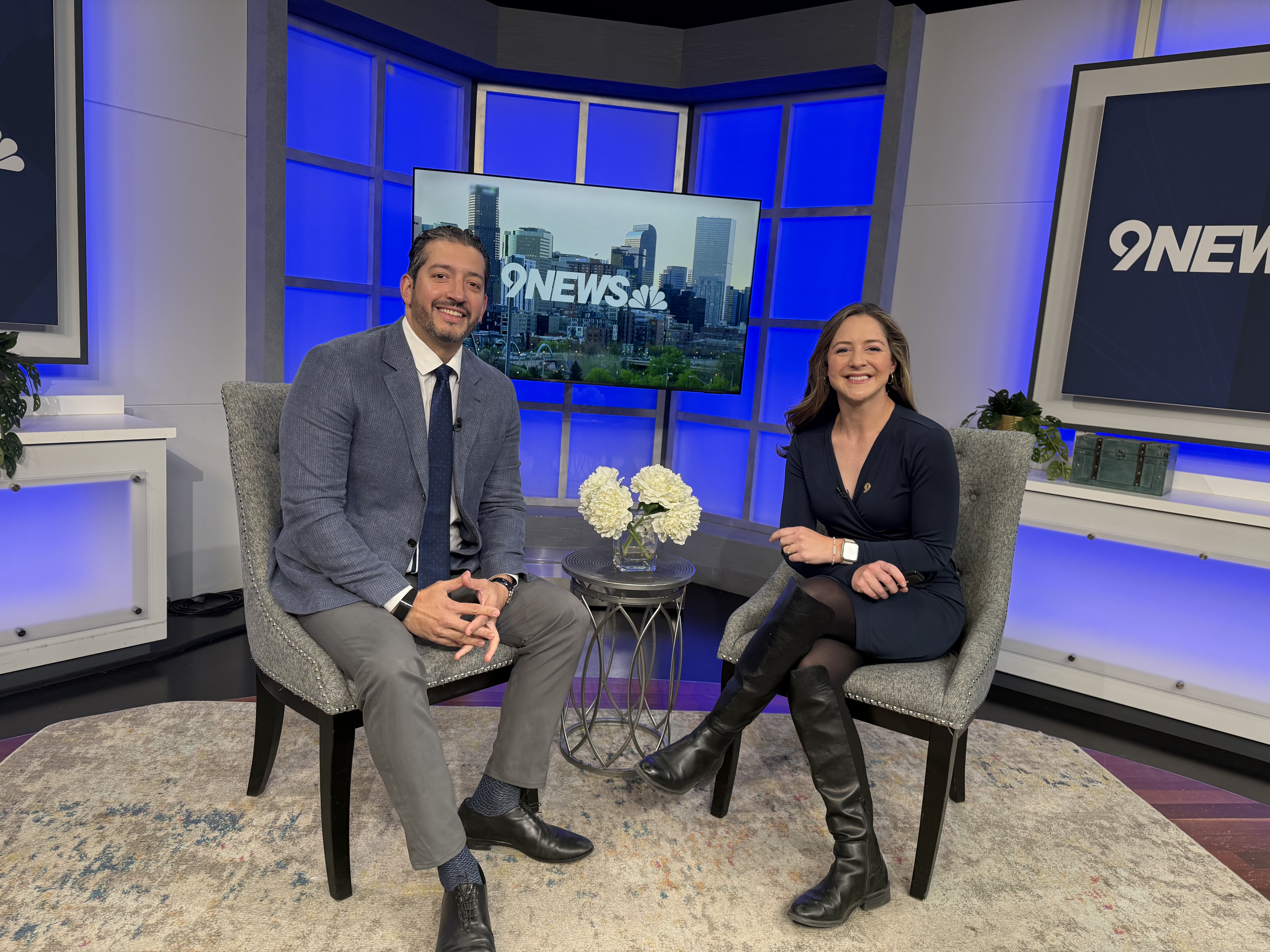 Dr. Raul Gosthe with the host smiling for a picture on the set of 9News.