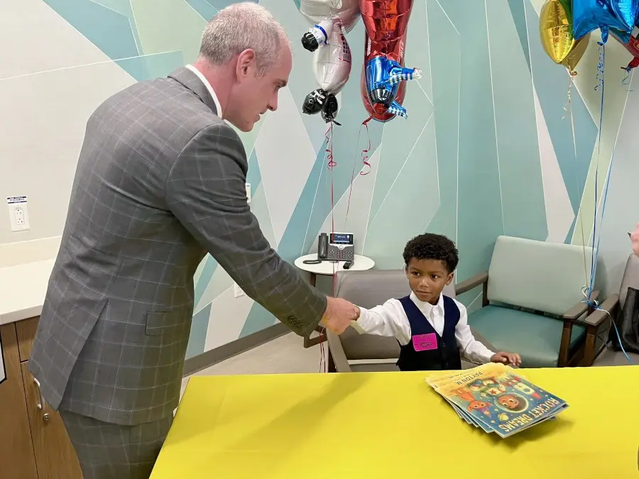 Hospital executive shakes hands with seated young boy at table with books.