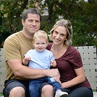 Emily, her husband and their son, Jonah, smile while sitting together on a patio couch. 