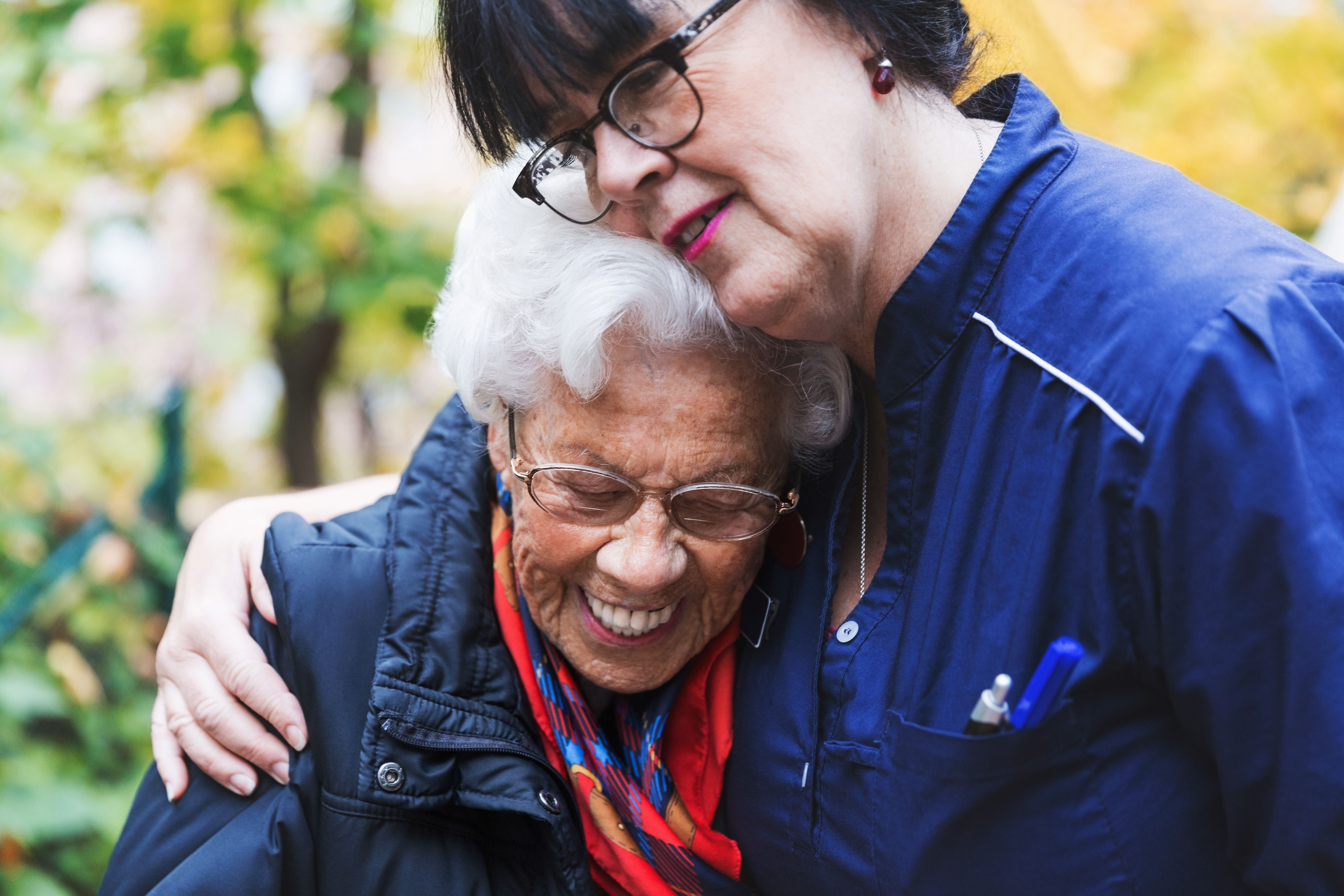 Caretaker embracing senior woman in park.