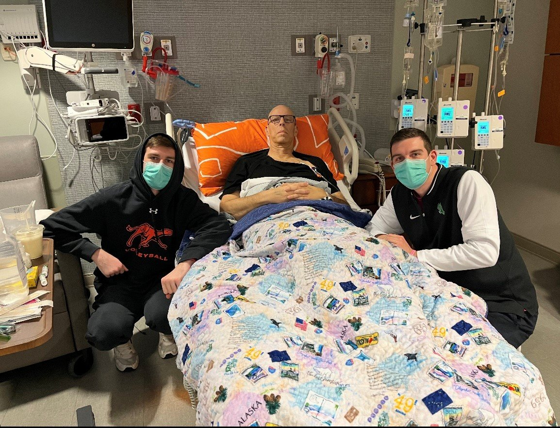 Wayne with his sons at his beside pose for picture in hospital room.