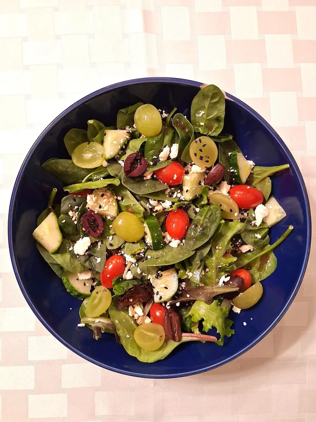 A blue bowl filled with salad, on top of a tablecloth.