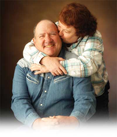 Raymond Yoak smiles while his wife, Janice, hugs him and kisses his cheek.