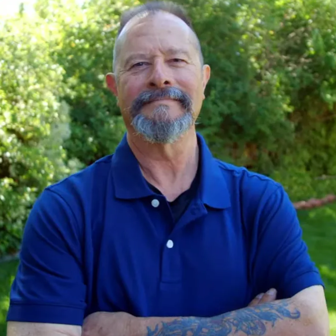 Spine surgery patient Mark Bernardini smiling with his arms folded outdoors.