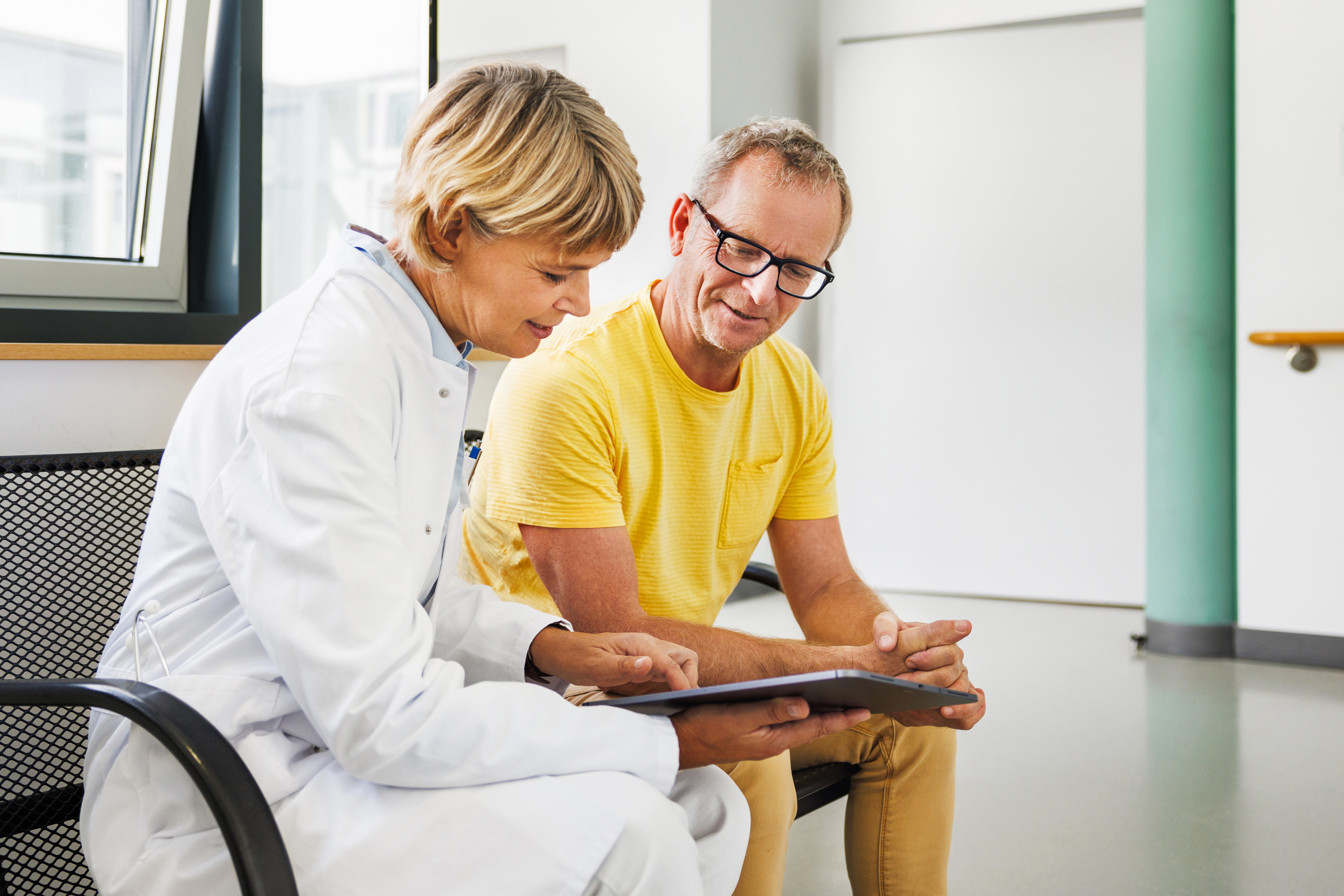 A physician and a patient smile while looking at a tablet together.