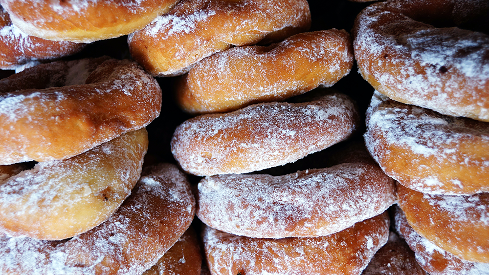 Up-close view of powered sugar covered donuts, lined up in rows.