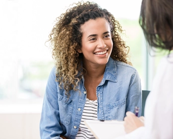 A smiling female patient attentively listens to her doctor.