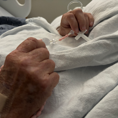 Patricia holds a rosary in her hands while lying in a hospital bed.