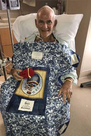 Gary Cox wearing a hospital gown, sitting in his hospital room, recovering.