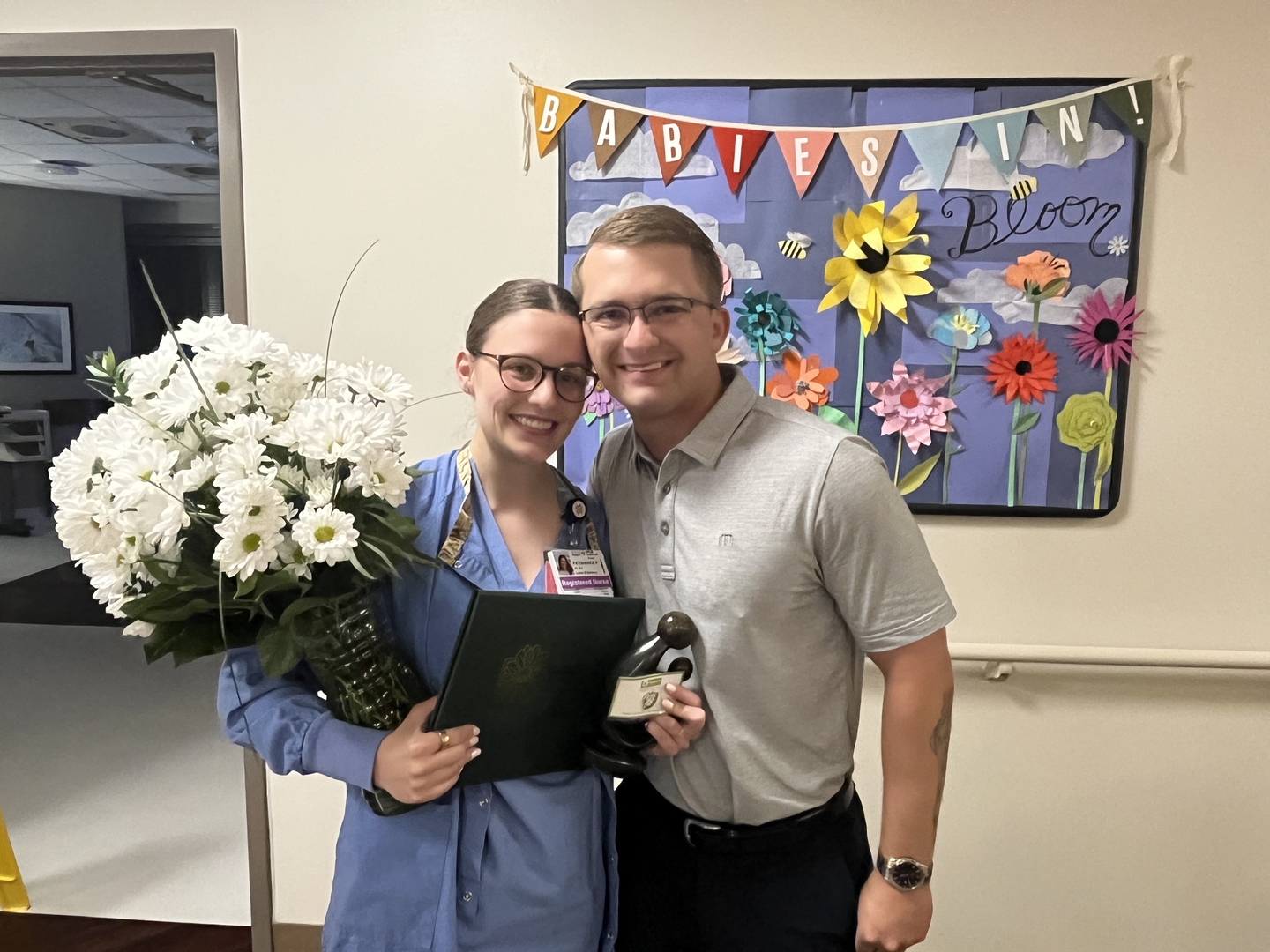 Paige Payshence, smiling and posing for a photo with a man, while holding her flowers and Daisy Award Certificate.