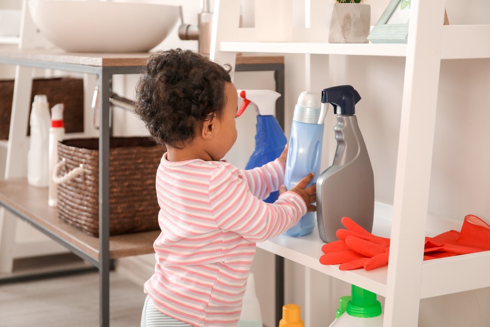 A toddler touching cleaning supplies on a shelf.