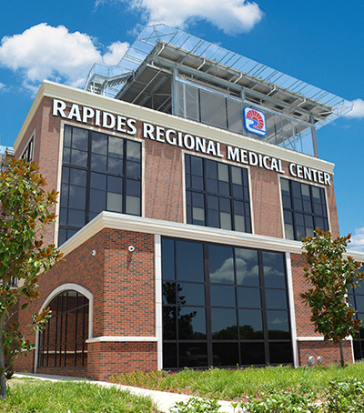 Exterior view of the Rapides Regional Medical Center with facility name featured prominently near top of structure with trees and grass in the foreground. 