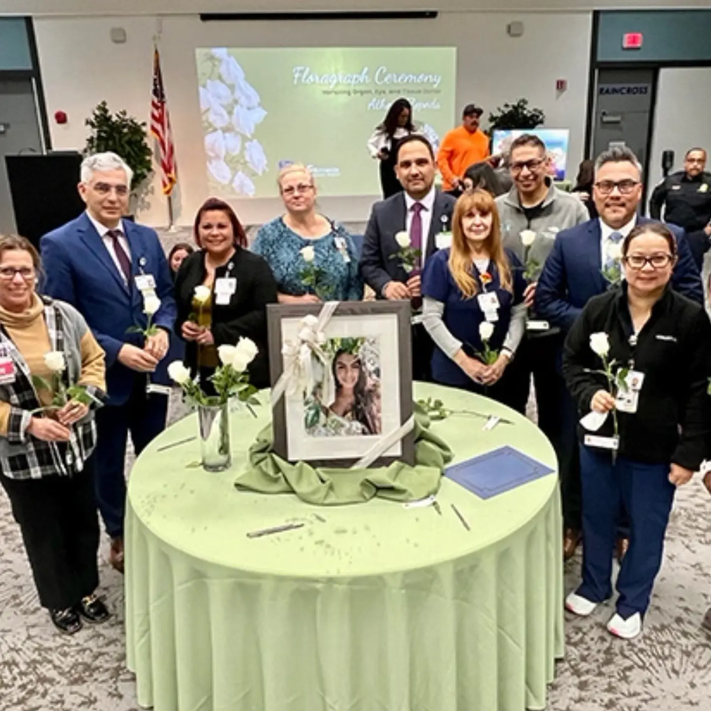 Antúnez family circling table, holding flowers, posing in front of honorary florograph for organ, eye and tissue donor Athena Zepeda, who is pictured in a photo.